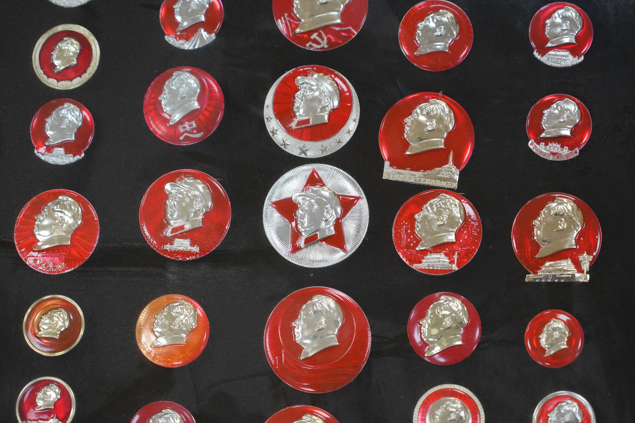A display case of Chinese red enamelled badges with the head of Chairman Mao, 72 x 85cm